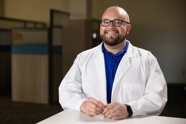 student wearing a labcoat smiles for a photo 