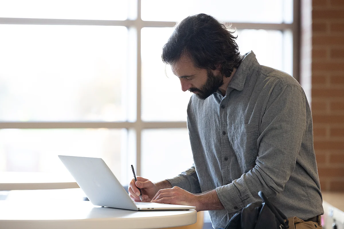 Man takes notes while working on a laptop.