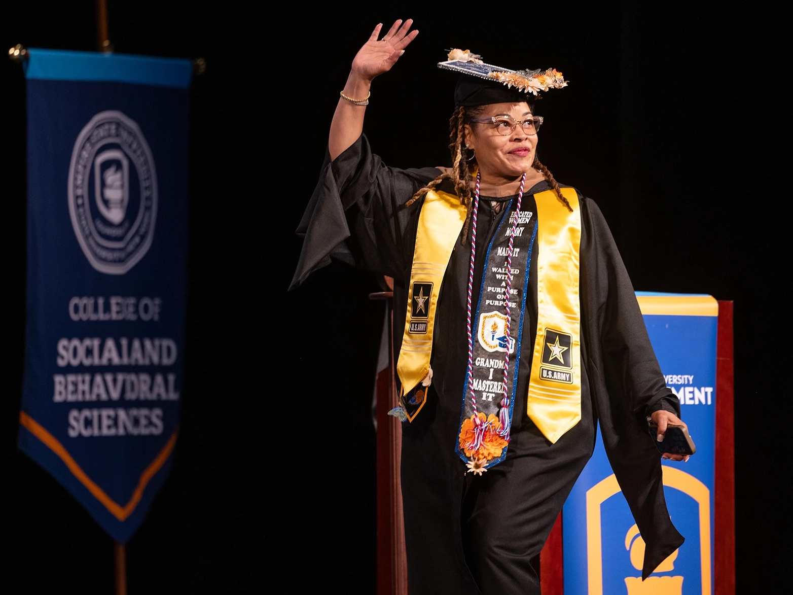 Student waves to the crowd as they cross the stage during graduation