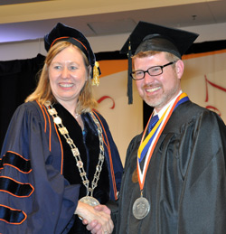 Acting President Meg Benke with student speaker and Chancellor’s Award for Student Excellence recipient Sean Coffman immediately after Coffman was presented with the college medallion.