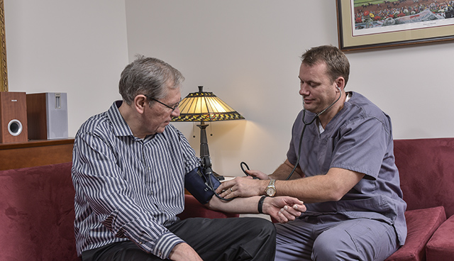 Stat Staff Professionals Founder and CEO David Theobald ’13, ’17, at left wearing medical scrubs, checks vital signs of former employee Ruffin Pauszek.